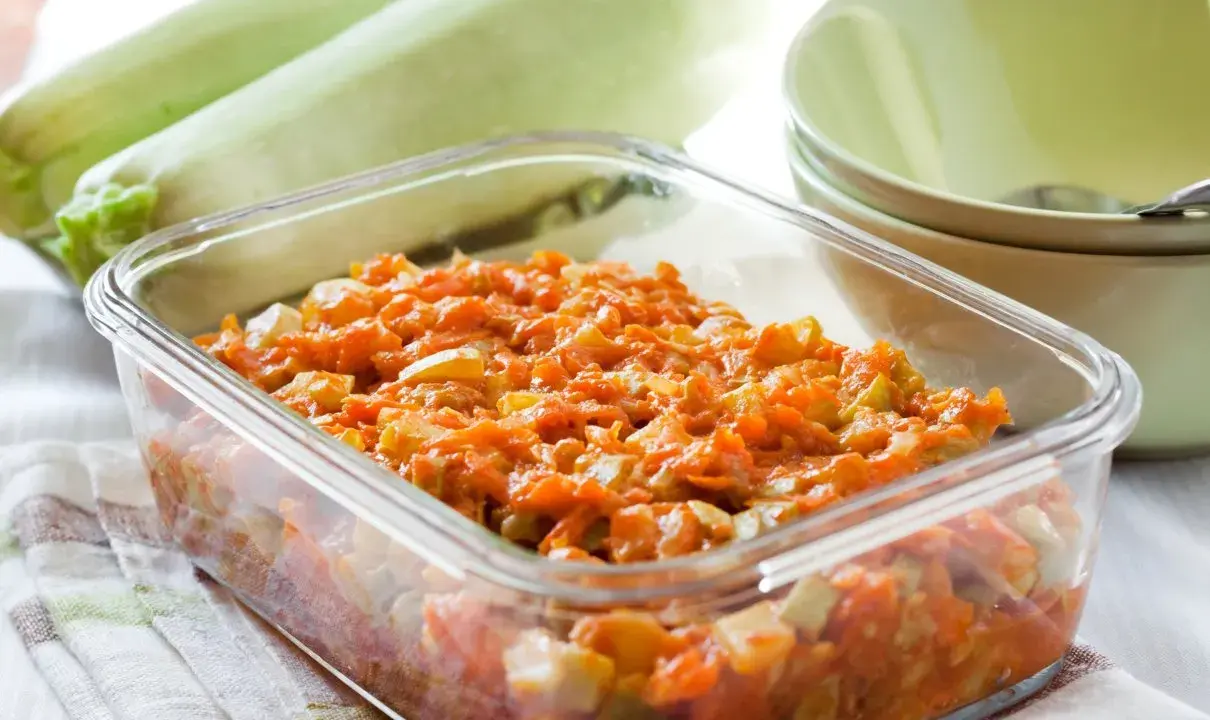 Pyszny bigos z cukinii w szklanym naczyniu, obok świeże cukinie i miseczki.