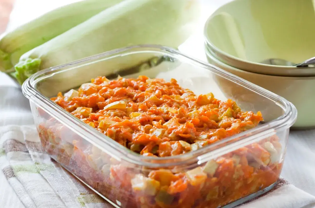 Pyszny bigos z cukinii w szklanym naczyniu, obok świeże cukinie i miseczki.