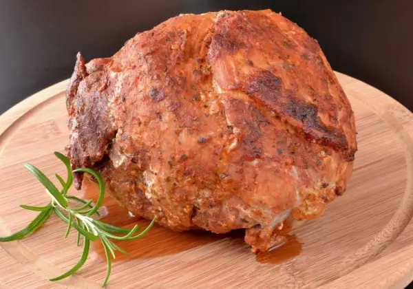 Pieczona szynka z ziołami, która wygląda jakby była przygotowana z użyciem marynaty do szynki. Gałązka rozmarynu dodaje aromatu.