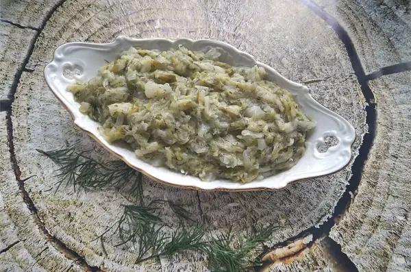 Pyszna kapusta zasmażana z koperkiem, podana w ozdobnej misie na tle drewnianej tekstury.