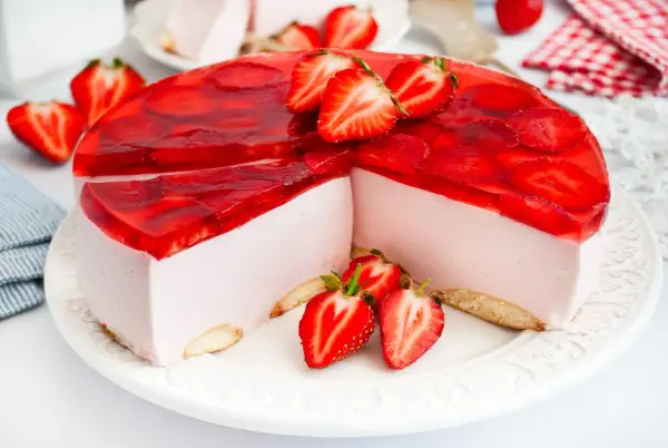 Pyszny sernik na zimno z mascarpone, udekorowany galaretką i świeżymi truskawkami. Idealny na letnie popołudnie.